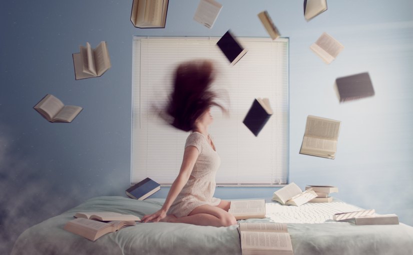 Woman kneeling on bed surrounded with books and papers and flying books she has tossed in the air.